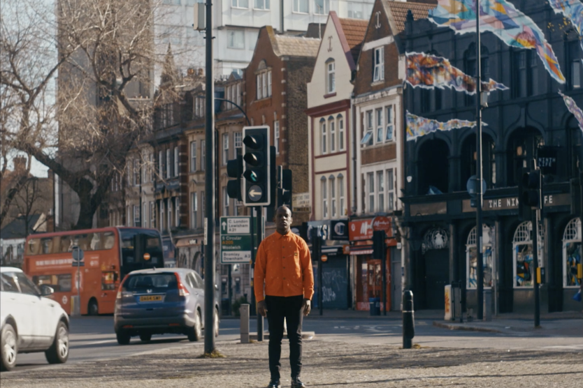 The image shows Love Ssega, who is standing on a street.