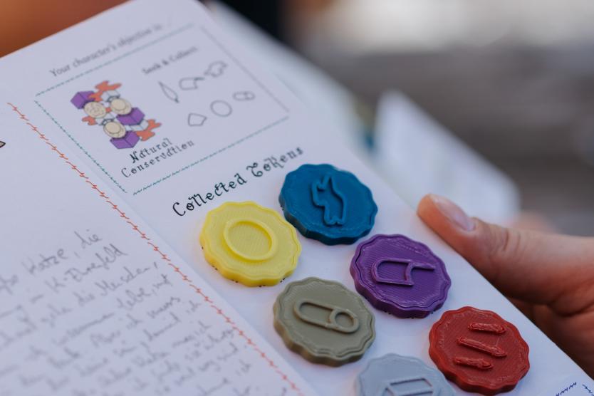 Das Bild zeigt ein Spielbrett mit handschriftlichen Notizen und mehreren farbigen Token, die gesammelt wurden, darunter gelbe, blaue, lila, rote und grüne.