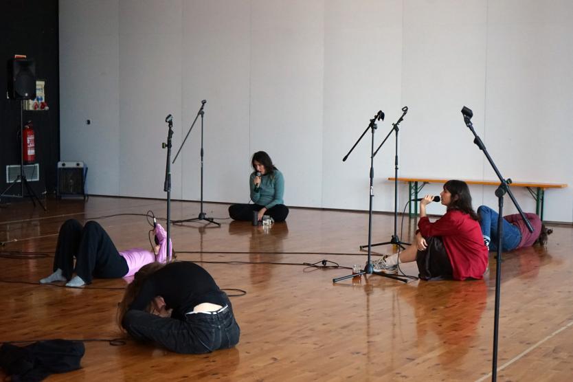 Eine Gruppe von Menschen liegt und sitzt auf dem Boden eines Raumes mit Mikrofonen.