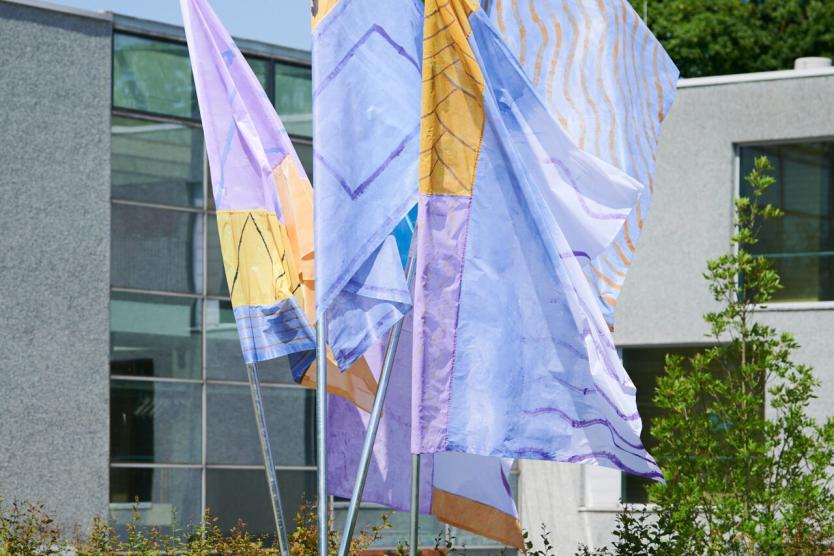Das Bild zeigt farbige Fahnen aus Stoff, die im Wind wehen und sich vor blauem Himmel entfalten.