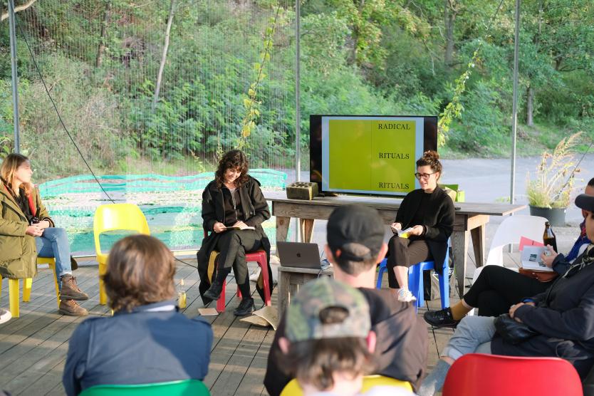 Das Bild zeigt ein Paneltalk mit 4 Frauen die diskutieren. Auf einem Screen ist die Aufschrift “RADICAL, RITUALS, RITUALS" zusehen.