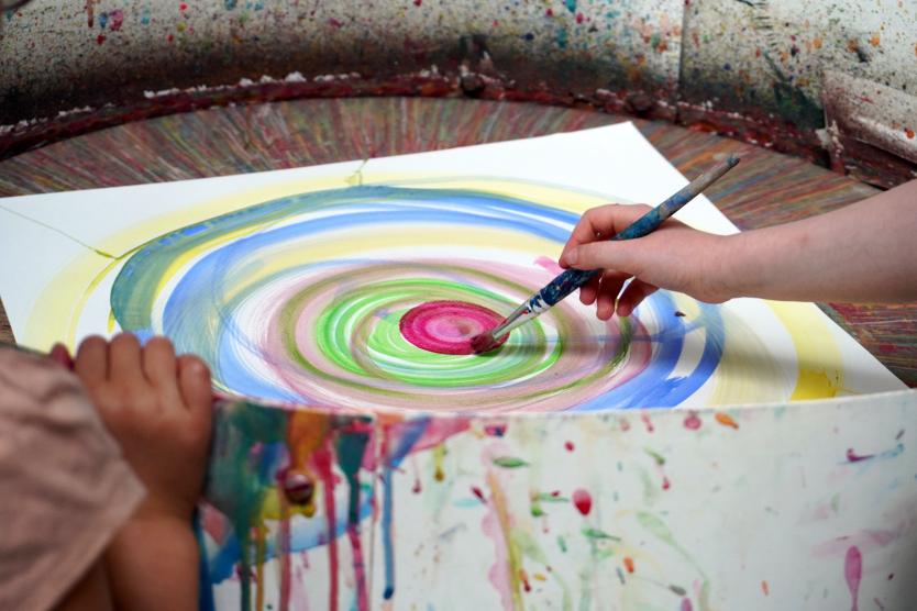 Ein Kind malt mit einem Pinsel bunte Kreise auf einem drehenden Blatt Papier.