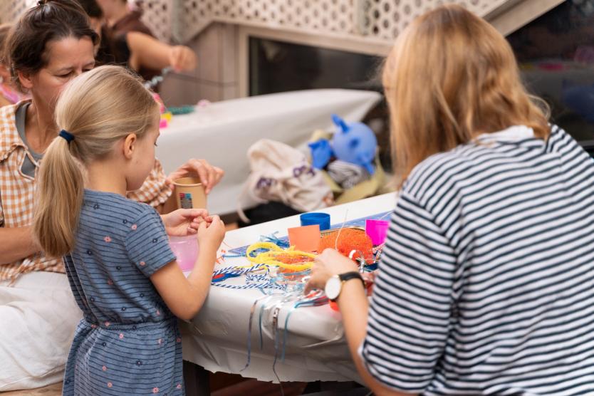 Kind und Erwachsene basteln gemeinsam an einem Tisch mit buntem Material.