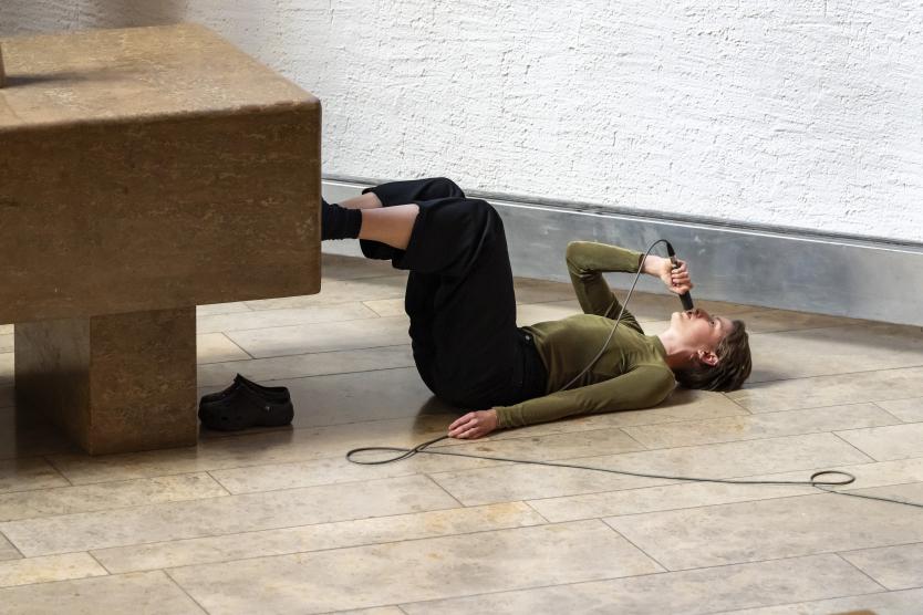 Eine Person liegt mit Mikrofon auf dem Kirchenboden, ein Fuß auf dem Altar, der andere barfuß. Eine ungewöhnliche Performance-Szene.
