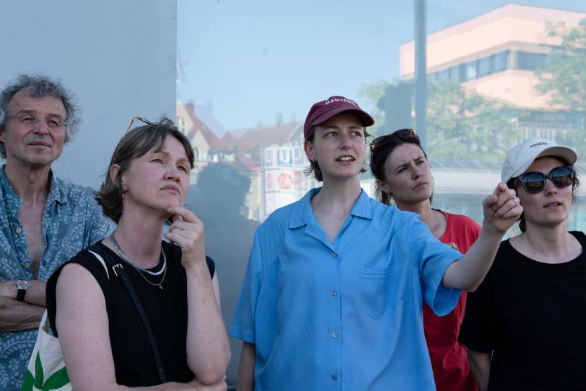 Eine Person in hellblauem Hemd ist umgeben von 4 Personen die der Person zuhören. Sie zeigt mit ihrer Hand in eine Richtung und die Personen folgen der Richtung mit ihrem Blick.