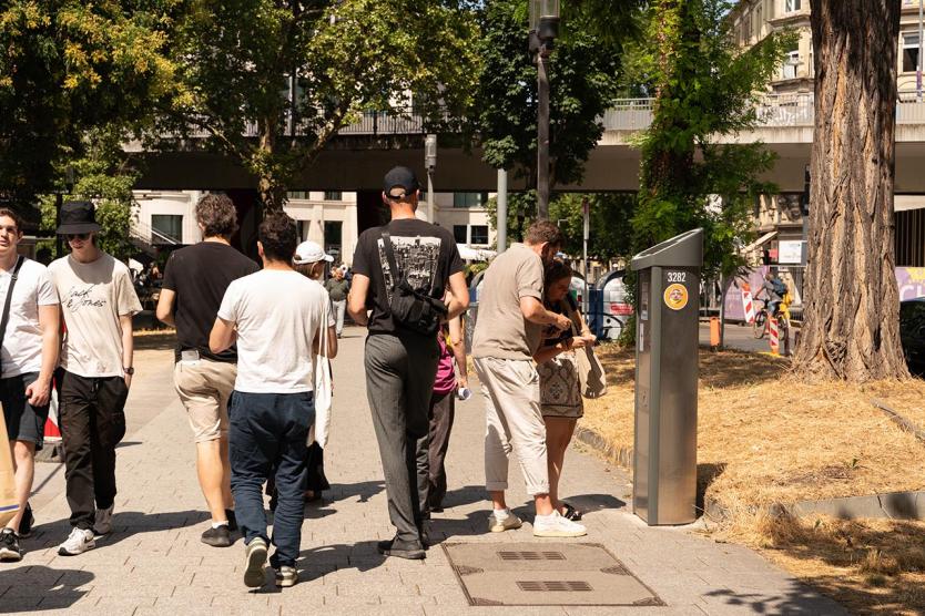 Eine Gruppe von Menschen bewegt sich bei Sonnenschein durch die Stadt – konzentriert, teils im Gespräch, teils mit Blick auf Details im öffentlichen Raum. Ein gemeinsamer Stadtrundgang als kuratorische Praxis.
