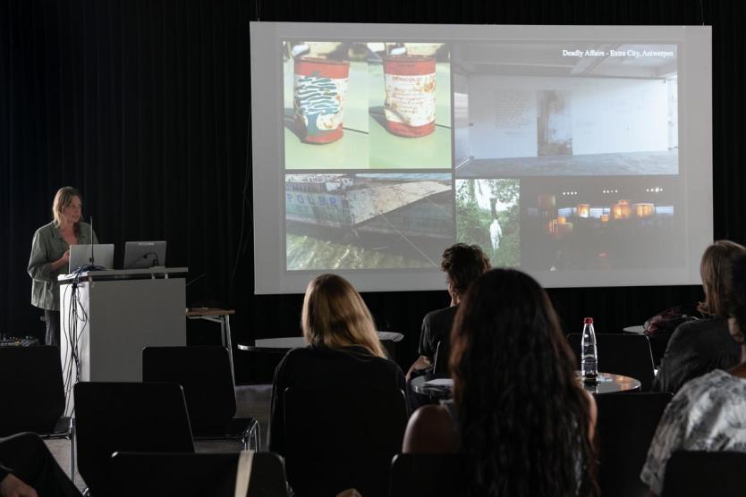 Vortrag vor projizierten Bildern, Publikum im abgedunkelten Raum.