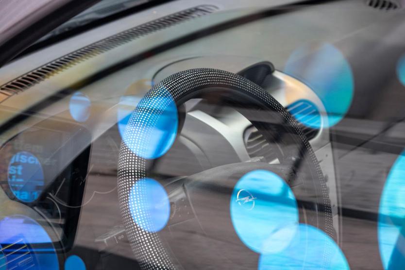 Nahaufnahme eines Lenkrads hinter Windschutzscheibe, darüber Reflexionen blauer Kreise.