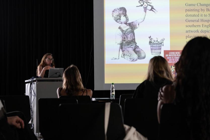 Vortrag mit Projektion einer Illustration von Banksy und Text zu feministischer Theorie im pandemischen Kontext.