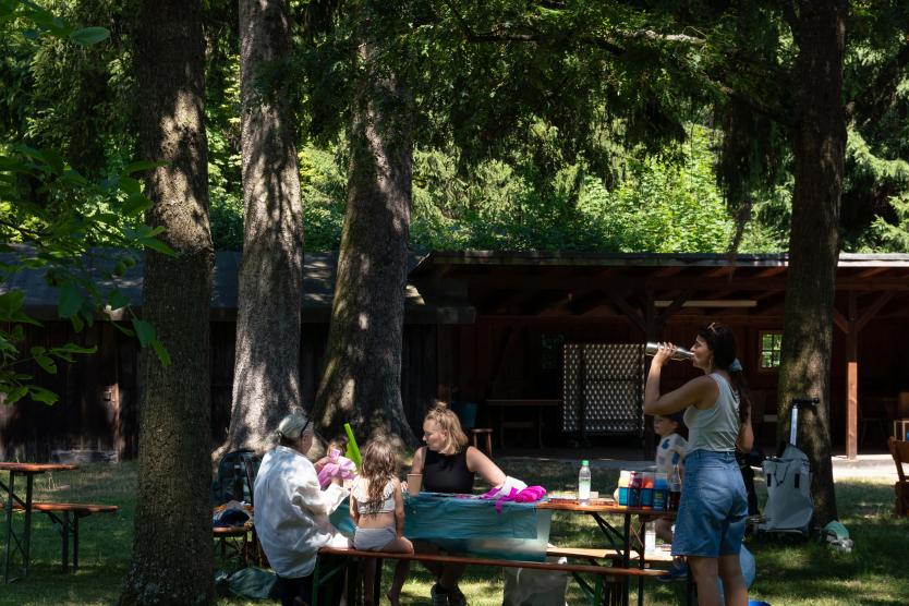Eine Gruppe von Personen ist um einen Tisch versammelt, umgeben von Bäumen und Natur und sie basteln zusammen mit buntem Papier.
