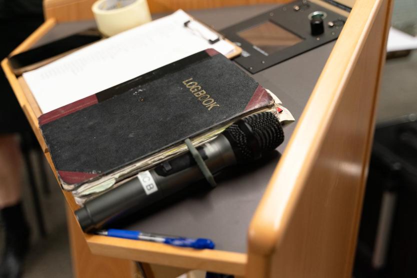 Nahaufnahme eines Rednerpults mit Mikrofon, Logbuch, Klemmbrett, Stift und Klebeband.