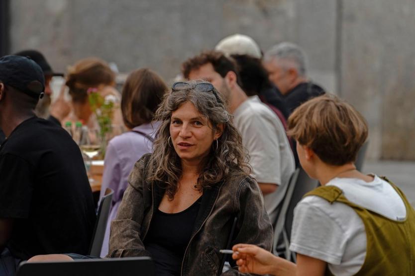 Zwei Personen sitzen am Tisch und sind im Gespräch. Sie sind umgeben von anderen Menschen die ebenfalls essen und im Gespräch sind.